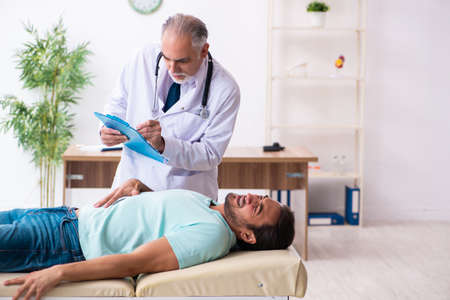 Injured young man visiting old doctorの写真素材