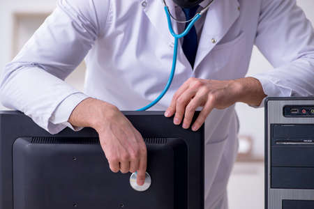 Young male doctor with stethoscope repairing computerの写真素材