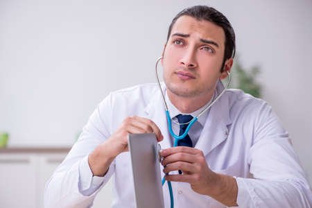 Young male doctor with stethoscope repairing computerの写真素材