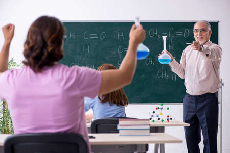 Old chemist teacher and two students in the classroom