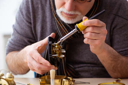 Old male watchmaker working in the workshop