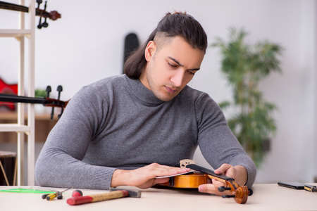 Young male repairman repairing violinの写真素材