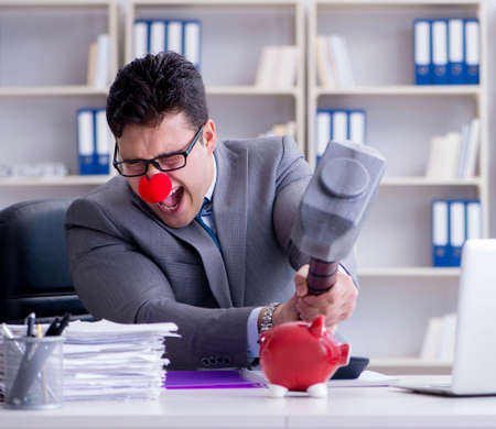 The clown businessman with a piggy bank and a hammerの写真素材