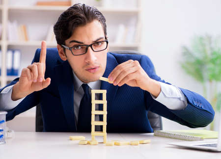Young businessman building domino tower in officeの写真素材