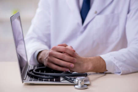 Young male doctor with stethoscope repairing computerの写真素材