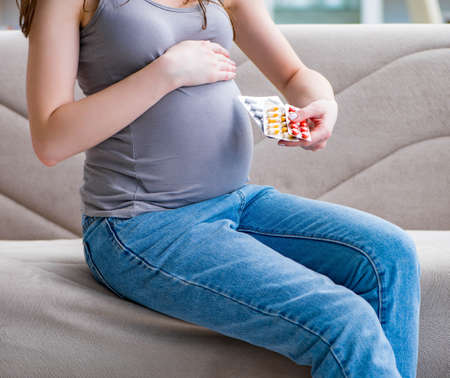 Pregnant woman with a belly tummy sitting on a sofa at homeの写真素材