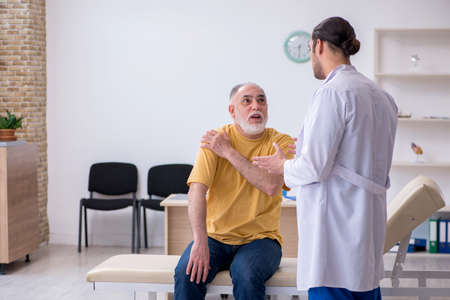 Old injured man visiting young male doctor chiropractor