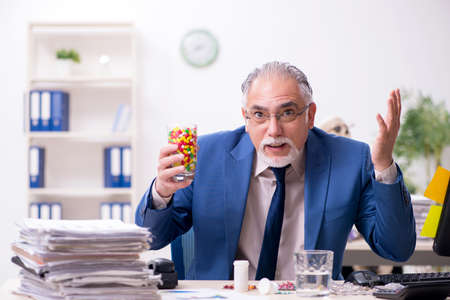 Old male sick employee working overtime in the officeの写真素材