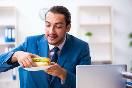 Young male employee having breakfast at workplaceの写真素材