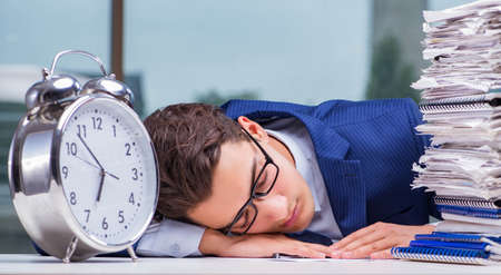 Businessman with pile stack of paper paperwork and an alarm clocの写真素材