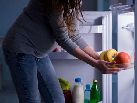 Pregnant woman near fridge looking for food and snacks at nightの写真素材