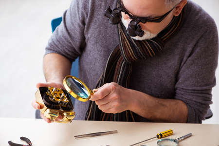 Old male watchmaker working in the workshop