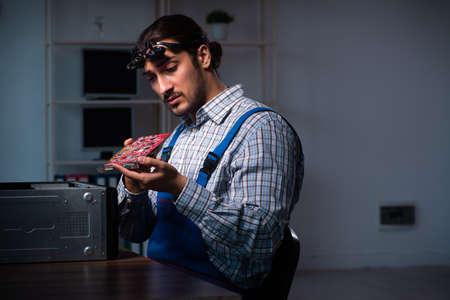 Young male technician repairing computer in workshop at night