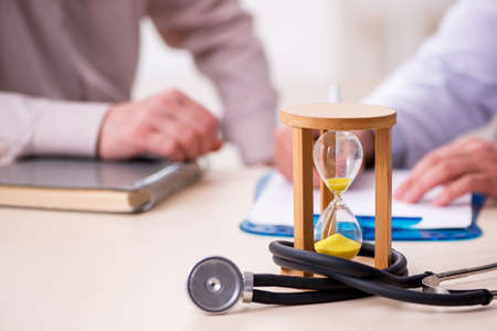 Old male patient visiting young doctor in time management concepの写真素材