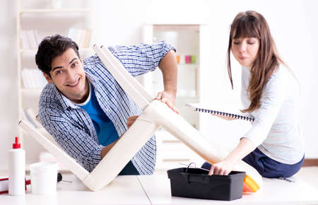Wife helping husband to repair broken chair at homeの写真素材