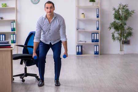 Young handsome male employee doing exercises in the officeの写真素材