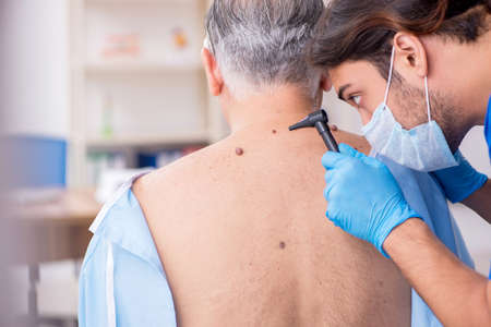 Old man visiting young male doctor dermatologistの写真素材