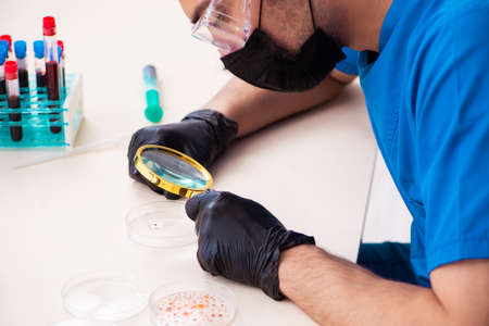 Young male biochemist testing blood samples in pandemic concept