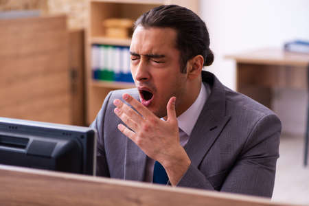 Young male employee unhappy with excessive work in the officeの写真素材