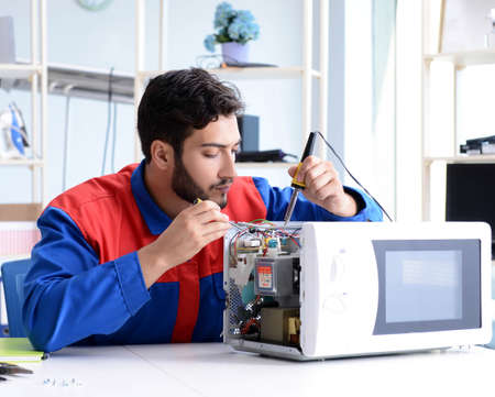 Young repairman fixing and repairing microwave ovenの写真素材