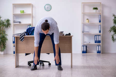 Young handsome male employee doing exercises in the officeの写真素材