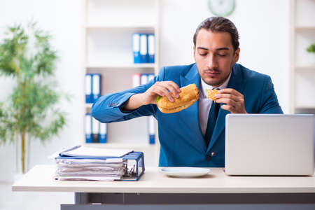 Young male employee having breakfast at workplaceの写真素材