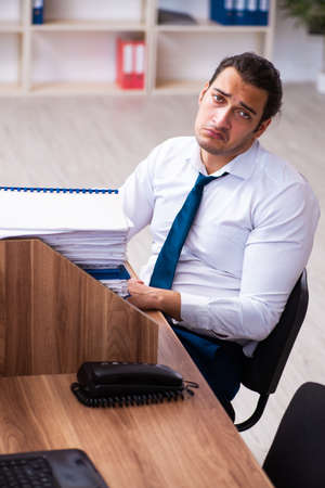 Young male employee unhappy with excessive work in the officeの写真素材