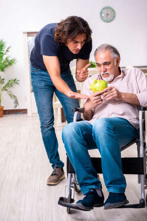 Old man in wheel-chair and young bad caregiver indoorsの写真素材