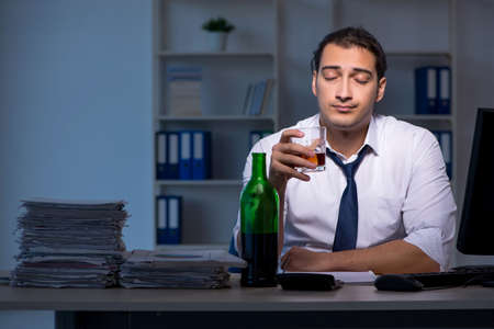 Alcohol addicted businessman working late in the officeの写真素材