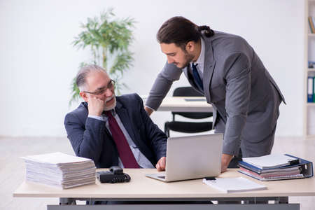 Old boss and his young assistant working in the officeの写真素材