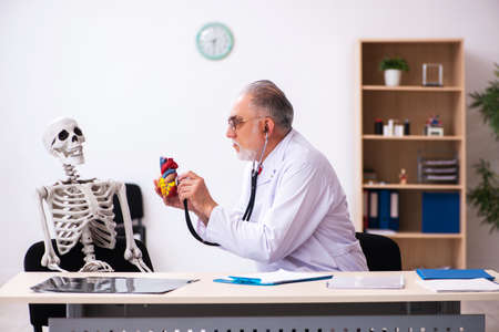 Old male doctor cardiologist and skeleton patient in the clinic