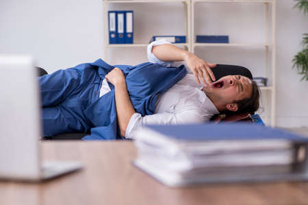Young male employee sleeping in the office on chairsの写真素材