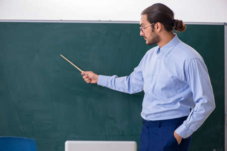 Young male teacher in the classroom in front of green board