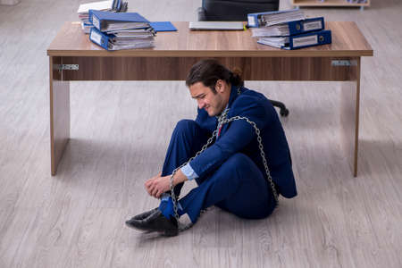 Chained male employee unhappy with excessive work in the officeの写真素材