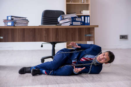 Chained male employee unhappy with excessive work in the officeの写真素材