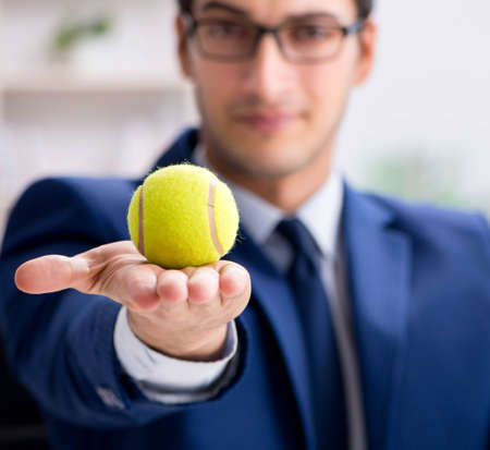 Young businessman with tennis ball working in officeの写真素材