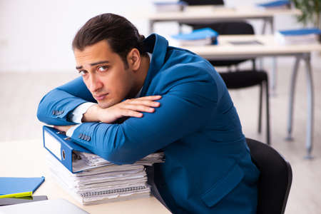 Young male employee unhappy with excessive work in the officeの写真素材