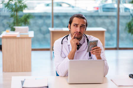 Young male medic holding banknote in the clinicの写真素材
