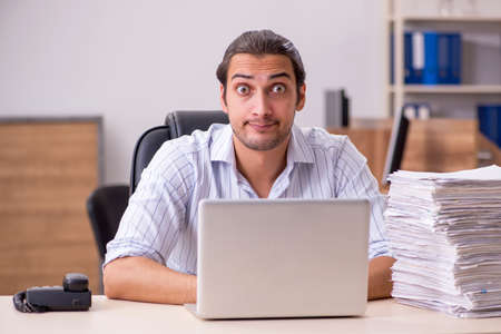 Young male employee and many paperwork in the office