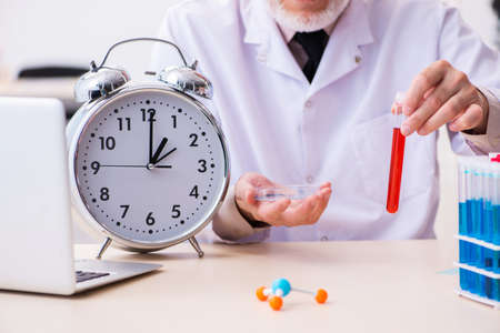 Old male chemist in time management conceptの写真素材