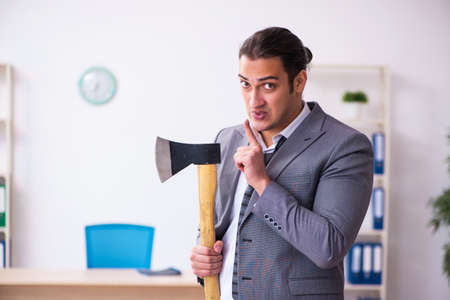 Young employee angry with excessive work holding hatchetの写真素材