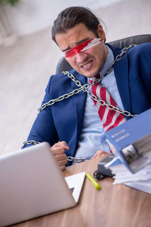 Chained male employee unhappy with excessive work in the officeの写真素材