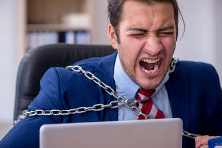 Chained male employee unhappy with excessive work in the officeの写真素材