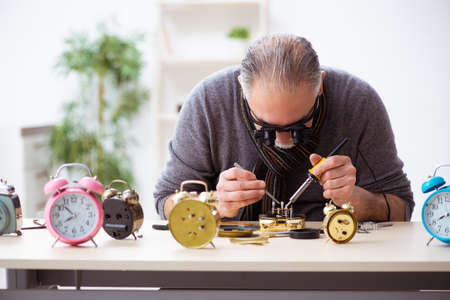 Old male watchmaker working in the workshop