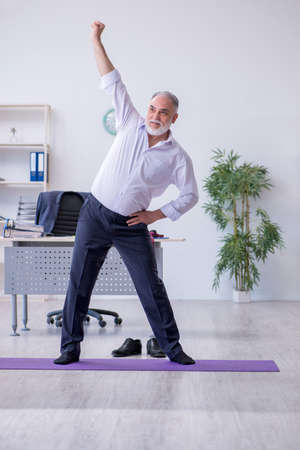 Aged male employee doing physical exercises during breakの写真素材