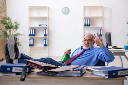 Old male employee drinking alcohol in the officeの写真素材