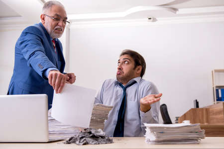 Young male employee and old boss burning papers at workplaceの写真素材