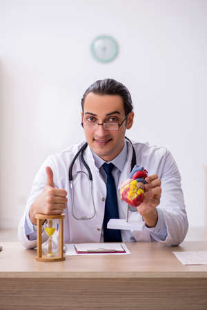 Young male doctor cardiologist in time management conceptの写真素材
