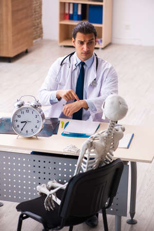 Young male doctor and skeleton patient in time management concepの写真素材