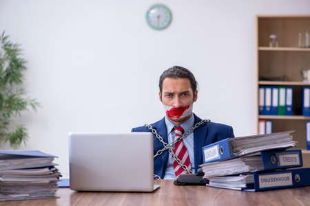 Chained male employee unhappy with excessive work in the officeの写真素材